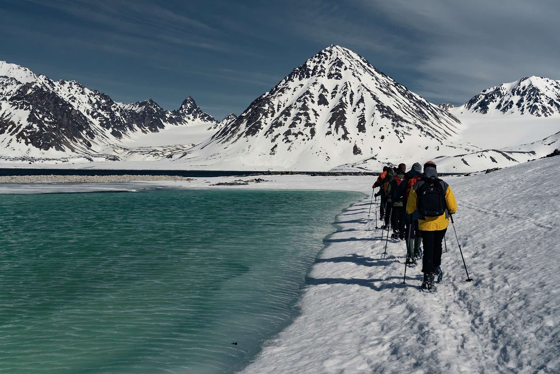 Een groep wandelaars doorkruist besneeuwd terrein langs een rustig meer, omringd door een winterlandschap.